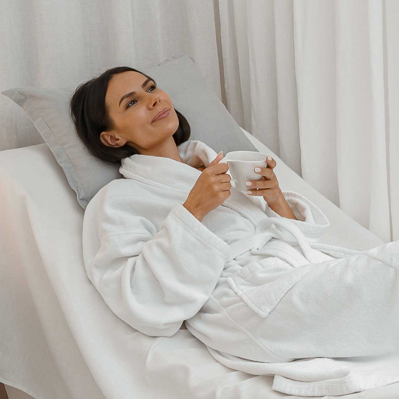 Woman relaxing in a white robe with a cup at a spa