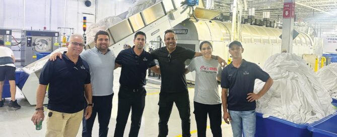 Elavo CEO Luis Aguilar poses for a photo with colleagues inside a commercial laundry facility.